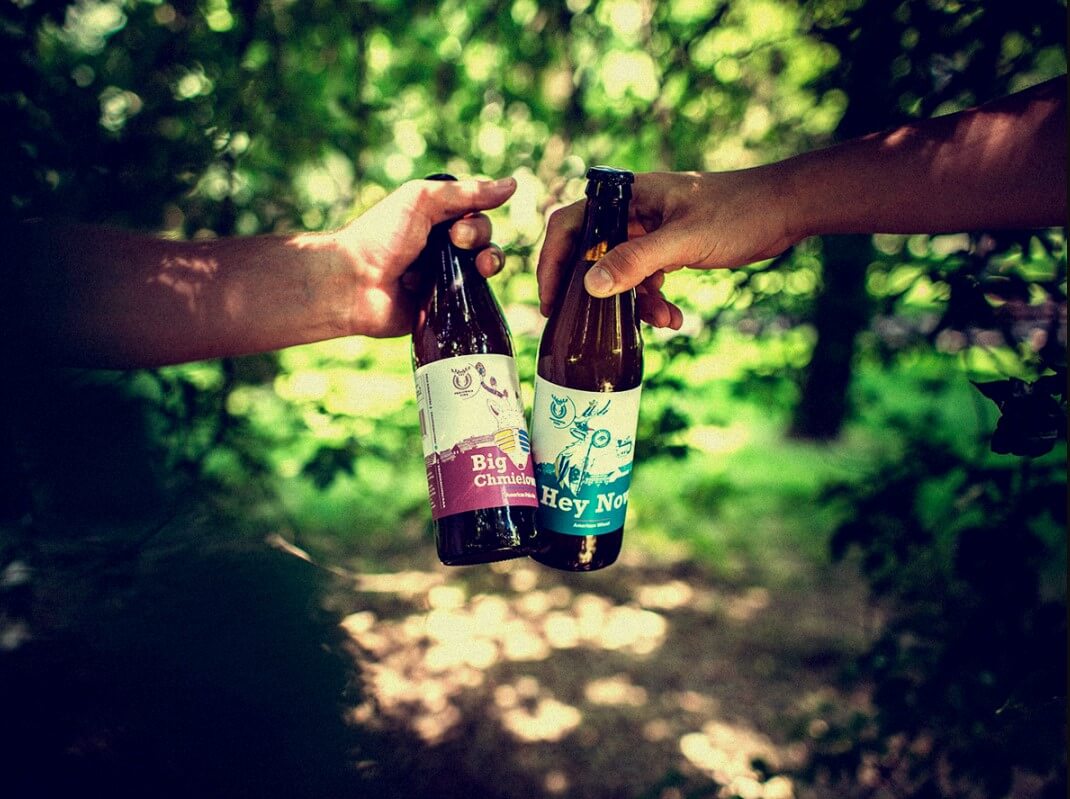 Dwie osoby stukające się butelkami piwa w lesie